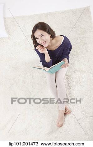 Stock Image - a woman sitting on a carpet reading a book. Fotosearch
