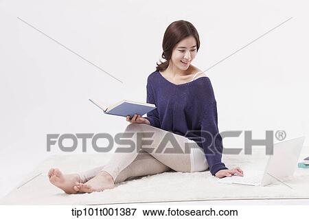 Stock Photo - a woman sitting on a carpet reading a book. Fotosearch