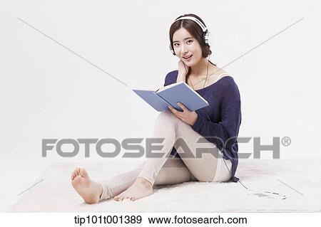 Stock Photo - a woman sitting on a carpet reading a book listening to a music . Fotosearch