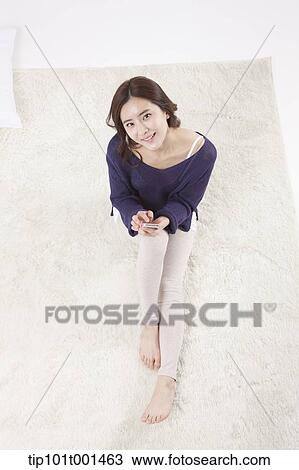 Stock Image - a woman sitting on a carpet using a mobile phone. Fotosearch