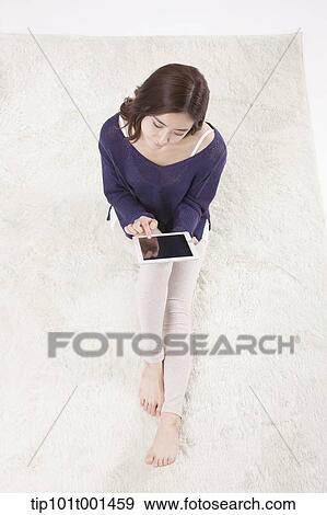 Stock Photo - a woman sitting on a carpet using tablet PC. Fotosearch