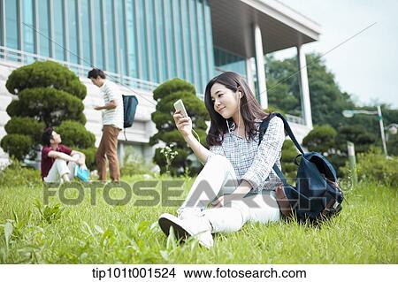Picture - a woman sitting on a grass listening to music. Fotosearch