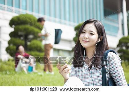 Stock Photo - a woman sitting on a grass listening to music. Fotosearch