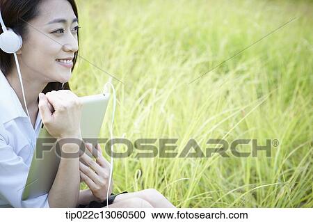 Stock Image - a woman sitting on the grass listening to music. Fotosearch