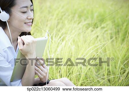 a woman sitting on the grass listening to music View Large Photo Image Stock Photo - a woman sitting on the grass listening to music. Fotosearch