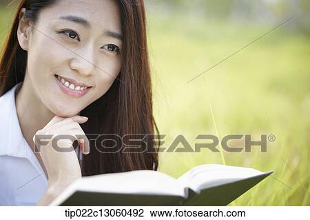 Stock Image - a woman sitting on the grass reading a book. Fotosearch