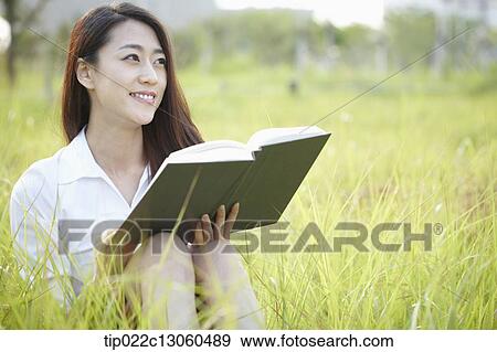 Stock Photo - a woman sitting on the grass reading a book. Fotosearch