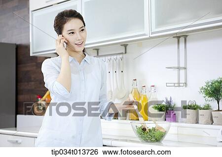 Stock Photograph - a woman talking on the phone while cooking. Fotosearch