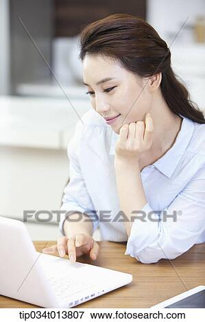 Stock Photo - a woman using laptop in the kitchen. Fotosearch