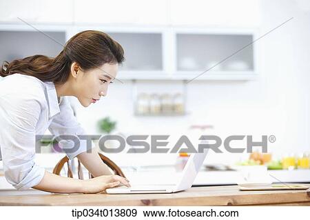 Stock Photo - a woman using laptop in the kitchen. Fotosearch