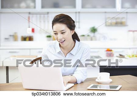 Stock Photograph - a woman using laptop in the kitchen. Fotosearch
