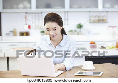 Stock Photography - a woman using laptop in the kitchen. Fotosearch