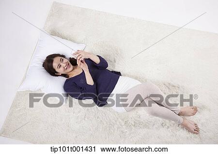 Stock Image - a woman using mobile phone while lying on a pillow. Fotosearch