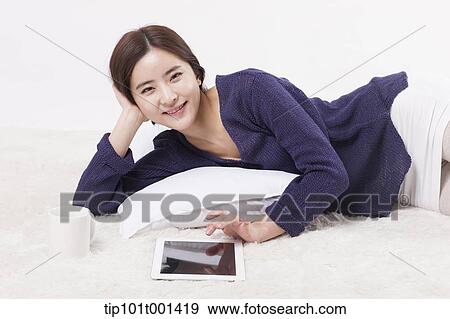 Stock Photo - a woman using tablet PC while lying on a pillow. Fotosearch