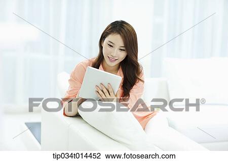 Stock Image - a woman using tablet PC white sitting on a couch . Fotosearch