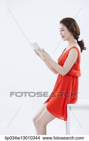 Picture - a woman with an orange dress leaning on a table. Fotosearch