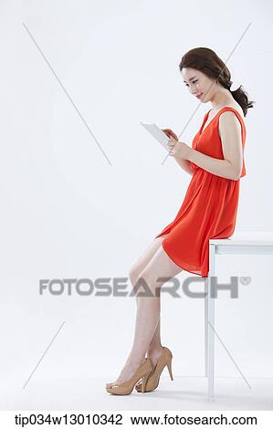 Stock Image - a woman with an orange dress leaning on a table. Fotosearch