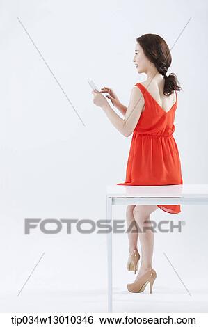 Stock Photograph - a woman with an orange dress leaning on a table. Fotosearch