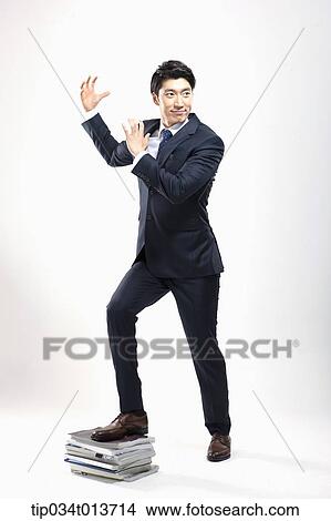 Picture - businessman posing while stepping on a pile of newspapers. Fotosearch