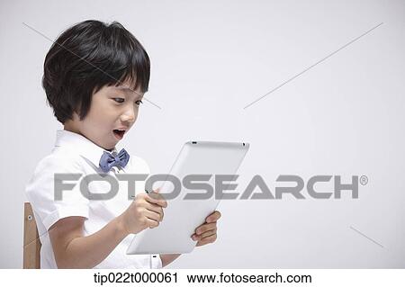 Stock Image - close up shot of a boy using tablet PC on a chair. Fotosearch