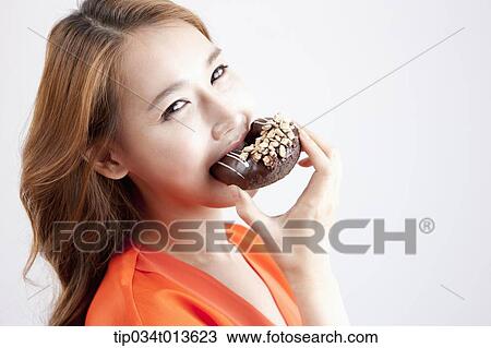Stock Image - close up shot of a woman eating chocolate doughnut. Fotosearch