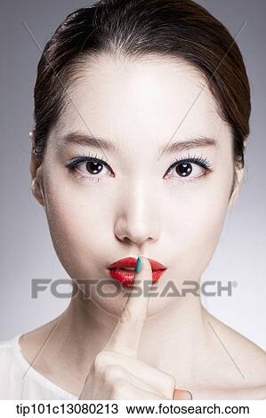 Stock Image - close up shot of a woman with a finger in her red lips. Fotosearch