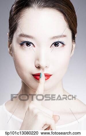Stock Image - close up shot of a woman with a finger in her red lips. Fotosearch