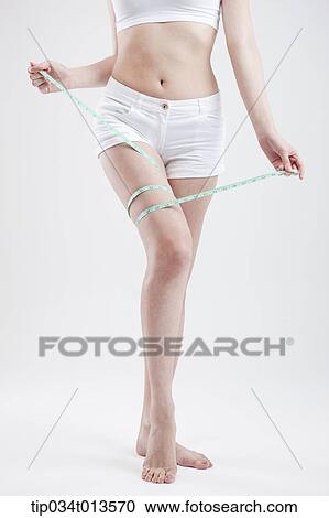 Stock Image - close up shot of a woman with measurement tape around the thigh. Fotosearch