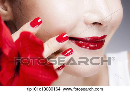 Picture - close up shot of a woman's red nails on a face with red lips. Fotosearch
