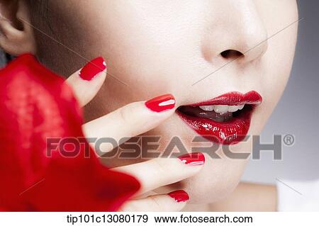 Stock Photo - close up shot of a woman's red nails on a face with red lips. Fotosearch