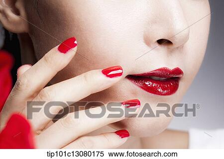 Stock Photography - close up shot of a woman's red nails on a face with red lips. Fotosearch