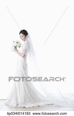Stock Image - full shot of a woman in wedding dress holding flower bouquet. Fotosearch