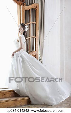Stock Image - full shot of a woman in wedding dress stepping up the stairs. Fotosearch
