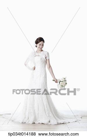Stock Photo - full shot of a woman in wedding dress holding flower bouquet. Fotosearch
