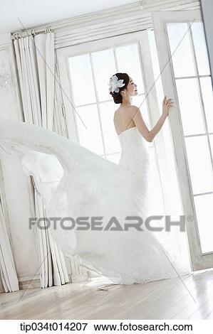 Stock Photo - full shot of a woman in wedding dress opening the window . Fotosearch