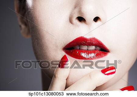 Stock Image - hand with red nail polish on woman's face with red lipstick . Fotosearch