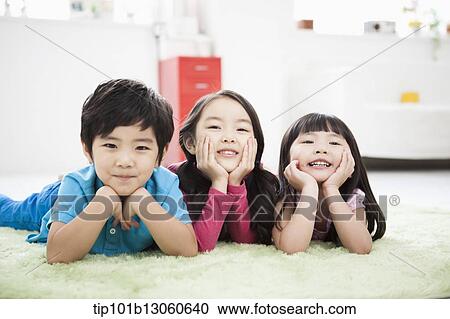 Stock Image - kids lying in the floor carpet with hands under their chin. Fotosearch