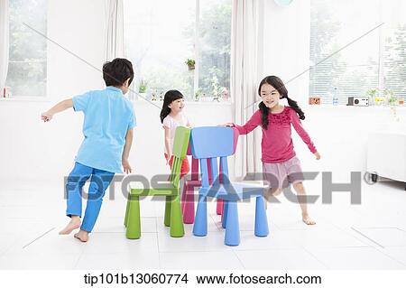 Picture - kids playing with different color chairs. Fotosearch