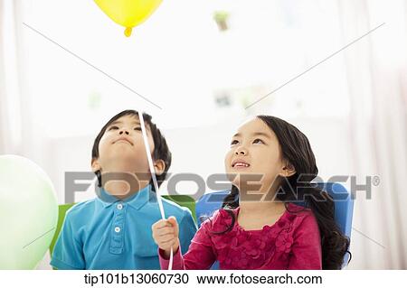 Stock Image - kids sitting next to each other holding balloons. Fotosearch