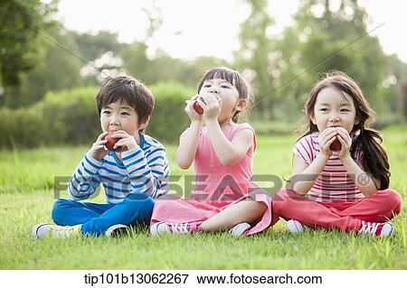 Stock Photo - kids sitting on the grass eating apples. Fotosearch