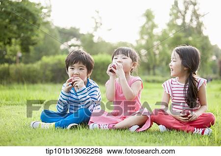 Stock Photo - kids sitting on the grass eating apples. Fotosearch