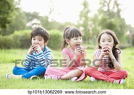 Stock Photo - kids sitting on the grass eating apples. Fotosearch