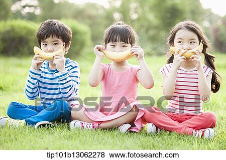 Stock Photo - kids sitting on the grass eating bananas. Fotosearch
