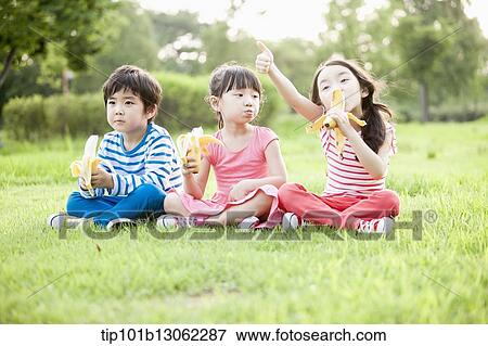 Stock Photo - kids sitting on the grass eating bananas. Fotosearch