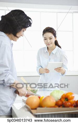 one woman cutting vegetables while the other woman uses tablet PC View Large Photo Image Stock Image - one woman cutting vegetables while the other woman uses tablet PC. Fotosearch