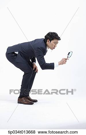 Stock Photo - side shot of businessman using magnifier bending down. Fotosearch