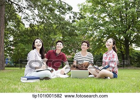 Stock Image - students sitting on grass studying with laptop together. Fotosearch