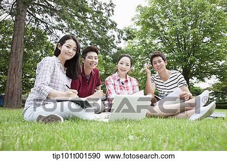 Stock Image - students sitting on grass studying with laptop together. Fotosearch