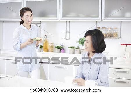 Stock Photo - two women having cup of coffee in the kitchen. Fotosearch