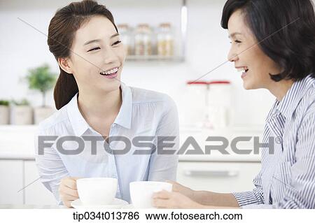 Stock Photograph - two women having cup of coffee in the kitchen. Fotosearch